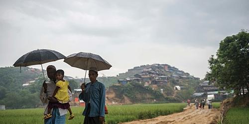 Rohingya Refugees walking with umbrellas holding a toddler